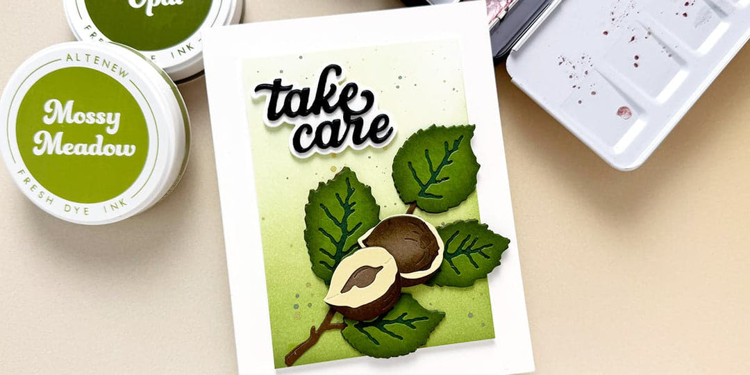 A handmade card with a die-cut sentiment "Take Care" and hazelnut branch on an ink-blended background