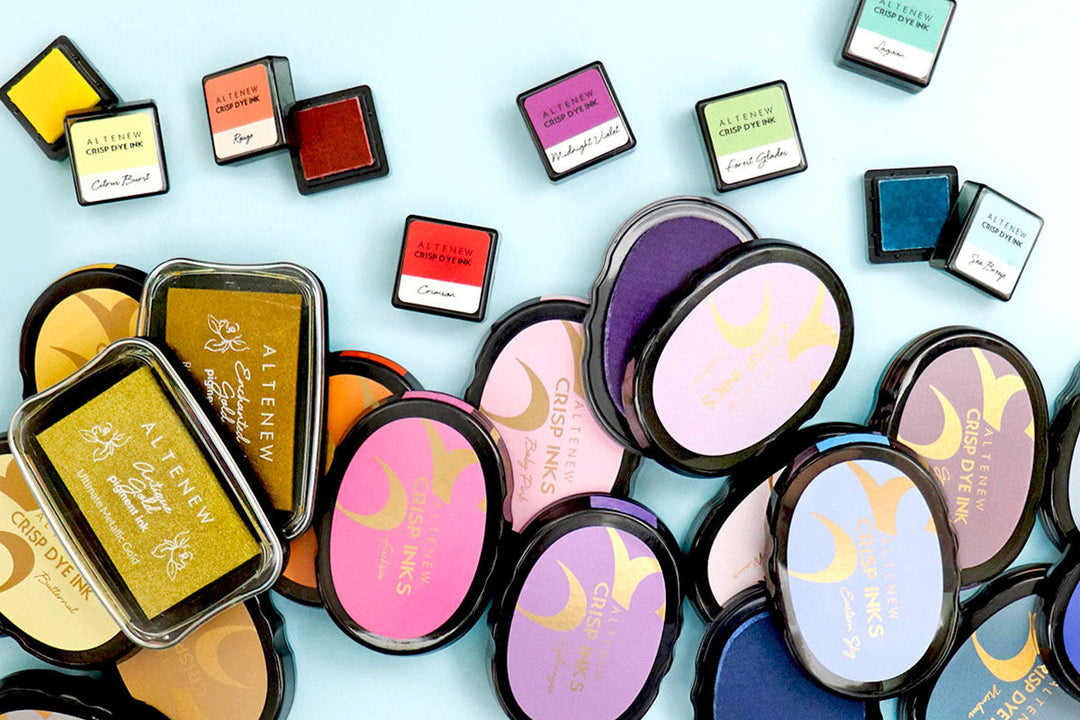 Altenew Crisp Dye Inks (Ovals), Mini Cubes, and Mixed Media Pigment Inks Laid Out on a Blue Surface