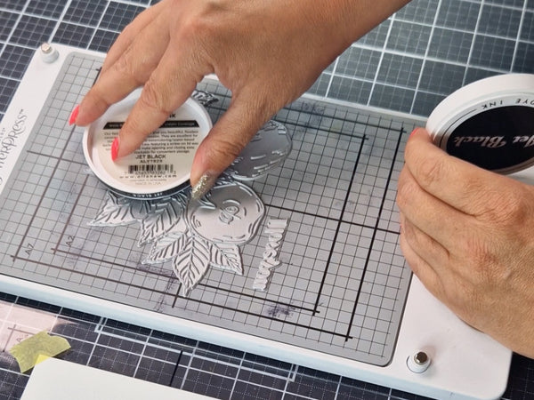 Secure your card panel to the clear top plate with low-tack tape, then gently ink the raised design.